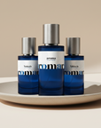 Three blue perfume bottles with silver caps on a beige plate against a beige background